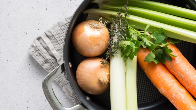 top down image of a pan containing with onions, carrots, celery, parsley and thyme